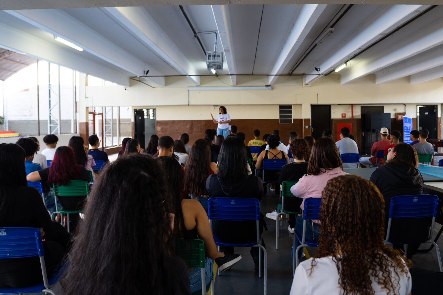 Um grupo de alunos sentados de constas com um professor em um palco na frente