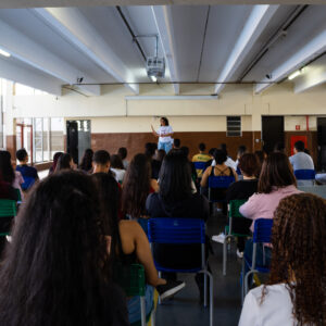 Um grupo de alunos sentados de constas com um professor em um palco na frente